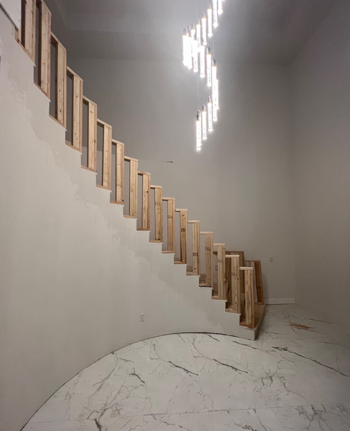 Curved wooden staircase with cascading pendant chandelier